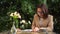 Young business woman sits in a cafe and writes in a notebook. Girl with coffee and a bun on the summer veranda.