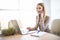 Young business woman speak at phone and using laptop at office. Look at camera.