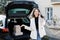 Young business woman standing at the car with parcels, coming home by car. The girl is standing and talking on mobile phone near