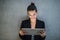 Young business woman with tablet standing against concrete wall in office.