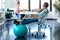 Young business woman taking a break and resting feet on the fitness ball in the office. In the background, her colleague working