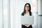 Young business woman working in her luxurious office holding a laptop standing against panoramic window with a view on business di