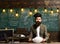 Young businessman with beard wearing suit and thinking. Blackboard background with many lightbulbs lit. Concept of doubt