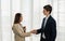 Young businessman and businesswoman shake hand together, smile, hold tablet, standing, wear suit. Young man and woman work