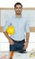 Young businessman in a casual business shirt and jeans holding yellow engineer hard hat standing with self-confidence and looking