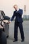 Young businessman in dark blue suit calling on cell phone next to his car