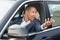 Young businessman driver sitting inside car driving hand outside standing in traffic jam shouting at vehicle at the back