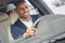 Young businessman driver sitting inside car holding steering wheel driving happy front outside view close-up