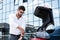 young businessman in eyeglasses rolling sleeves of white shirt near car trunk