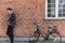 Young businessman going to work on bike commute using his mobile cellphone against city brick wall background. Happy