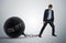Young businessman has chained big metal ball to his leg with debt written.