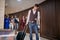 Young businessman pulling suitcase on wheels, looking at his cellphone with colleagues behind him