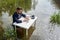 Young businessman sits waist-deep in a swamp at an office desk