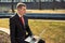 Young businessman sitting with a laptop on a park bench. guy in a suit with a red tie. freelance. remote work concept.