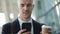 Young businessman standing near office building using smartphone with headphones and drinking coffee. Business man in