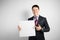 Young businessman in suit on gray background holding banner in his hands, poster placard with empty space for text