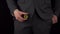A young businessman in a suit takes out a bitcoin coin from his pocket. The waist of a man is close-up on a black
