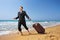 Young businessman in suit walking on a beach with his luggage