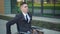 Young businessman in a suit in a wheelchair. A serious man rides in a wheelchair and looks at his watch against the