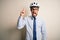 Young businessman wearing glasses and bike helmet standing over isolated white bakground pointing finger up with successful idea