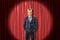 Young businessman wearing golden crown on red stage curtains background