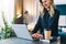 Young businesswoman in black blouse is standing indoor, working on computer. Girl freelancer, entrepreneur works at home