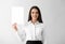 Young businesswoman with blank sheet of paper on light background