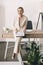 Young businesswoman with clipboard sitting on desk and laughing at camera