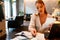 Young businesswoman doing paperwork and using laptop in restaurant