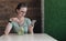 Young businesswoman in glasses sits in a cafe at table, drinks a beverage and uses a smartphone. Girl working, blogging