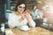 Young businesswoman in glasses and white sweater is sitting in cafe at table and using smartphone, working.E-learning