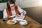 Young businesswoman in glasses and white sweater is sitting in cafe at table, working.Girl is looking at charts, graphs