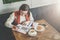 Young businesswoman in glasses and white sweater is sitting in cafe at table,working. Woman is looking at charts, graphs