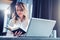 Young businesswoman in shirt is sits in office at table in front of computer and reads notes in notebook. Student