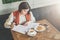 Young businesswoman is sitting in cafe at table, signing documents. Student is studying online, doing homework.