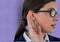 Young businesswoman wearing eyeglasses listening gossip against purple background