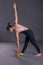 Young calm beautiful woman wearing black sportswear does stretching exercising using a  brick  on gray background in studio, full