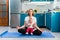 A young calm mother meditates in the kitchen while a nervous upset baby sits on her lap. The concept of yoga and meditation