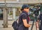 Young camerawoman with light professional video equipment on a tripod, sunglasses and black cap shoots a film