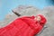 Young camper resting in sleeping bag on cliff near lake
