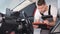 A young car mechanic of American appearance checks the technical condition of the car using a tablet.