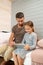 Young careful father sitting on bed next to his little daughter with touchpad