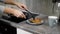 Young careful woman is taking pancakes from pan and putting on a plate on kitchen table in morning time