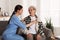 Young caregiver examining senior woman on sofa in room. Home health care service