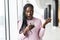 Young casual african woman shoked news from mobile phone in front of panoramic windows