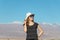 Young casual blond woman in hat and sunglasses looking away with snow covered mountains on the background