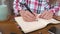 Young Caucasian attractive woman taking notes in her notebook while sitting in the kitchen at the table. Paper notebook