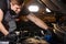 Young caucasian auto mechanic in a car service, checks a car, engine, carburetor