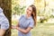 Young caucasian blond woman in a blue stripped summer dress playing hide and seek with her boyfriend in the park outdoors in a