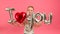 Young caucasian blonde boy holds in her hands red and silver inflatable balloon with inscription I LOVE YOU smiles and